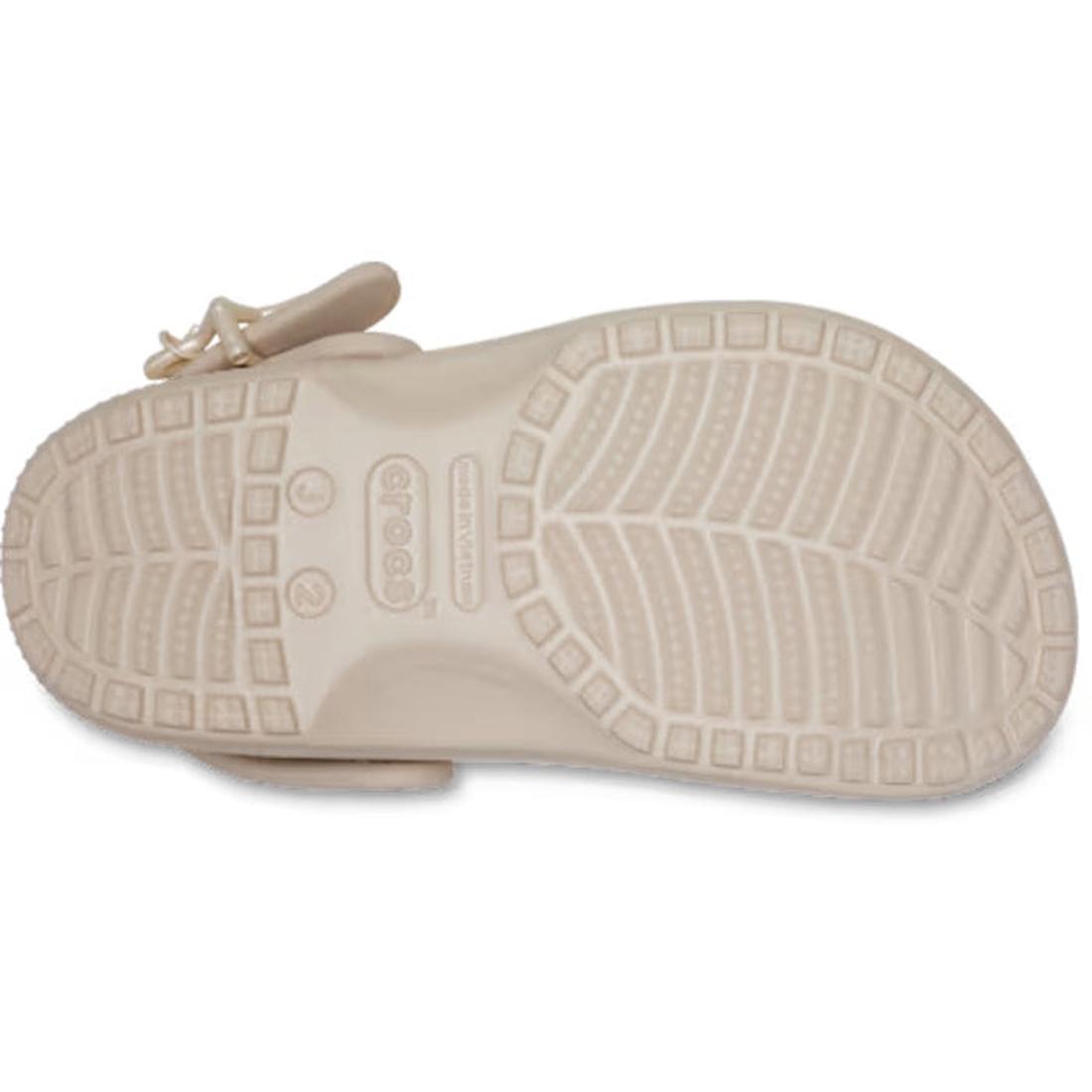 The image displays the beige-colored sole of the Crocs Kids - Classic Clog Star Buckle Frappe (Junior Youths Sizes), highlighting its textured tread pattern and the Crocs logo near the heel. Designed for ventilated comfort, this water-friendly sandal comb