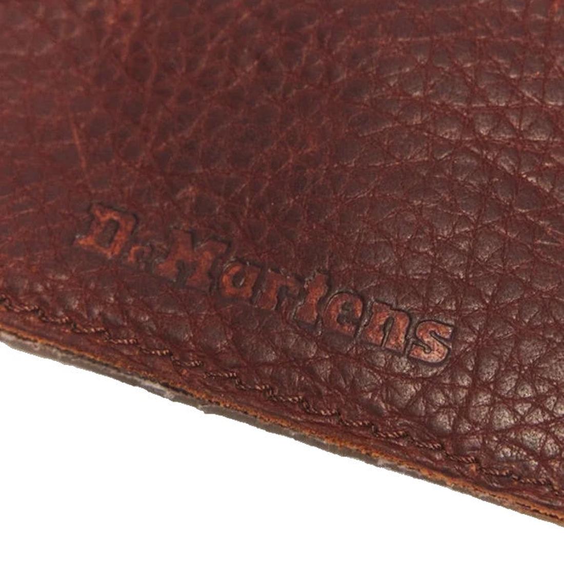 Close-up of brown textured Ambassador leather from the Dr Martens Cardholder Keyring Cashew Bag Charm, featuring the Dr. Martens logo embossed on the surface and partially visible stitching along the edge, reminiscent of a premium leather wallet., 1906657