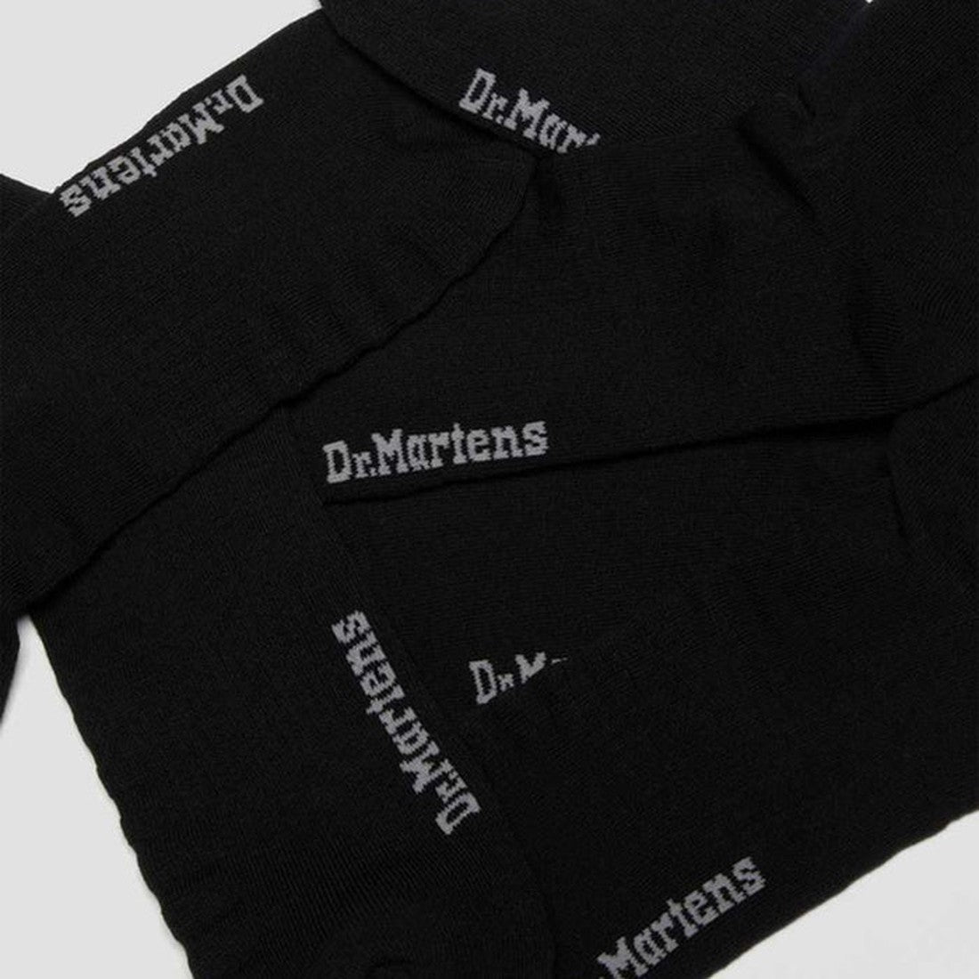 A close-up of three pairs of unisex black Dr Martens Double Doc Socks, each with the white Dr. Martens logo near the cuff. Designed for blister protection, these socks are arranged overlapping in a flat-lay display. 3 pair pack included., 190665563122, 19