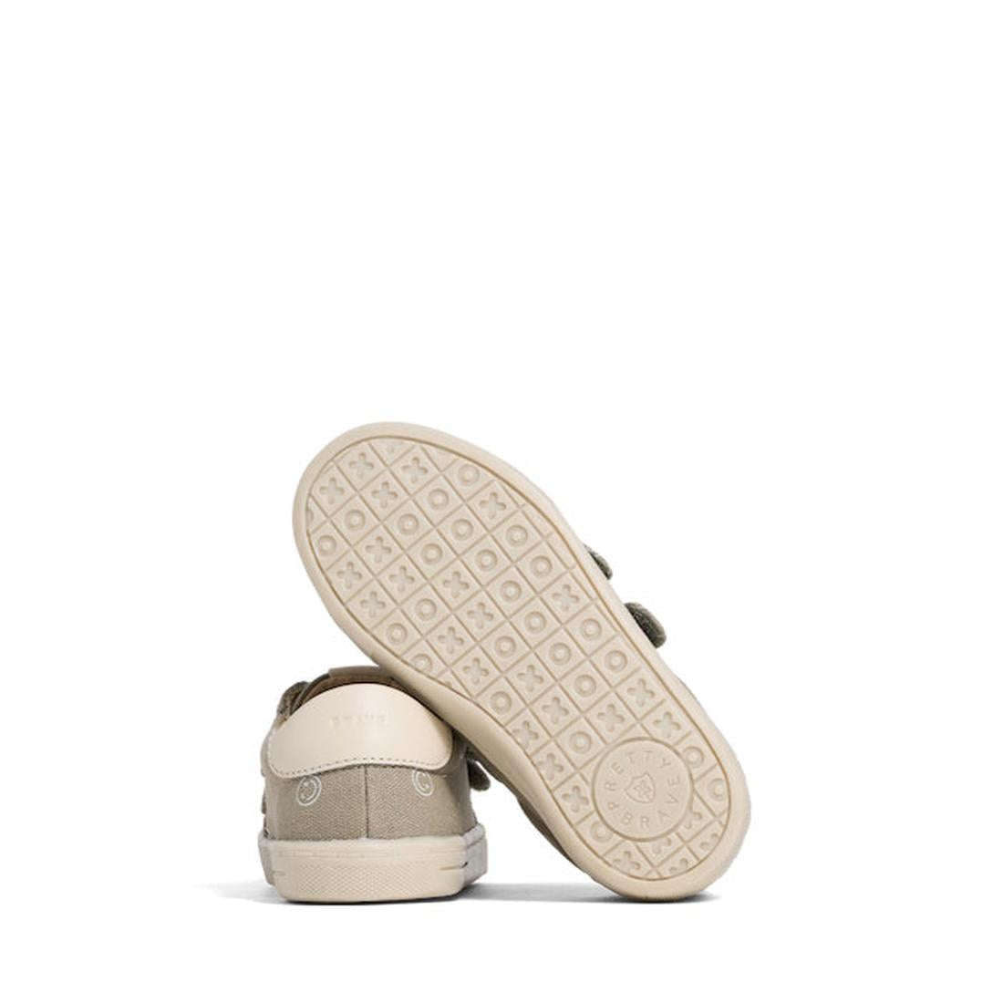 The Pretty Brave Otto Organic Canvas Trainer With Leather Toe Buffer in Khaki Smiley is displayed, featuring one upright shoe and one tilted to reveal the patterned sole. These sneakers offer a casual, minimalist design in organic cotton canvas., 40216, 4