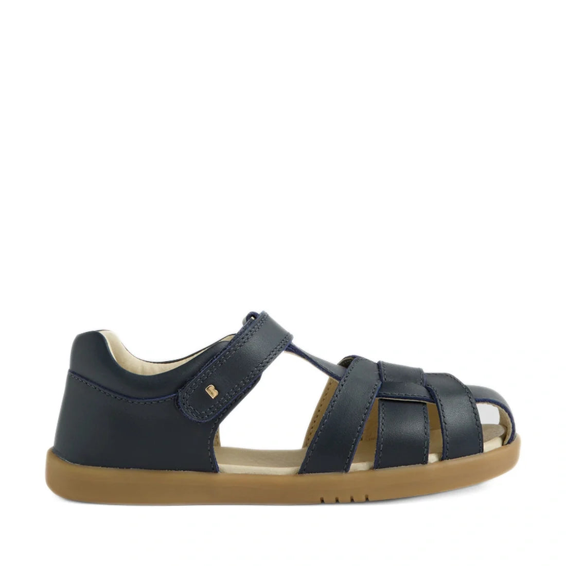 The Bobux Kids Plus KP Skip Twist Navy Closed Toe Sandal features a navy blue design with a tan rubber sole, Velcro strap, and open sides for enhanced breathability. Ideal as summer footwear, these children’s sandals are shown against a plain white backgr