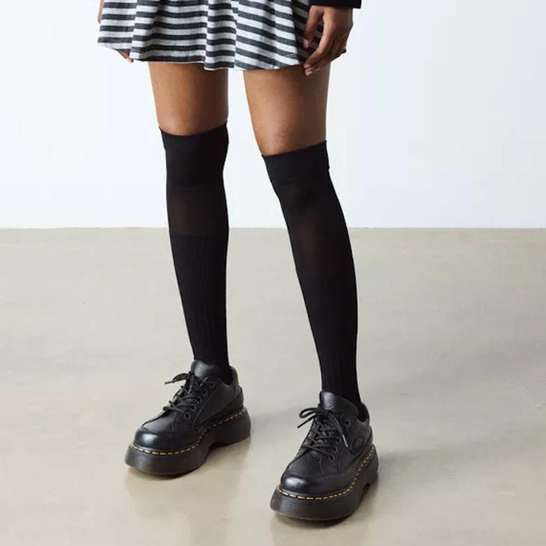 A person wearing a black-and-white striped skirt, black knee-high socks, and Dr Martens Buzz 5i Milled Nappa Black Leather 5 Eye Shoes stands on a light floor against a plain background., 51613, 190665702798, 190665702804, 190665702828, 51618, 51619