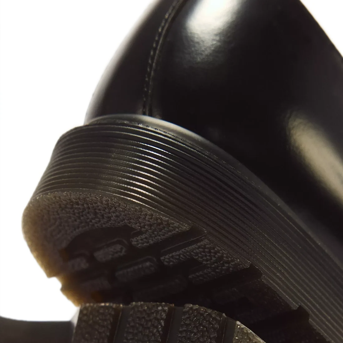 Close-up of the heel of the Dr Martens Mayfare Polished Smooth Leather Shoes Oxford 3 Eye Black, focusing on the ridged edge of the sole and textured tread. The white background highlights the shoe’s glossy finish and sturdy Goodyear-welted construction.,