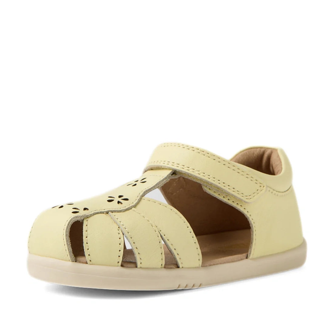The Bobux IWalk Holly Toddlers Sandal in Wax Yellow is a light yellow closed-toe sandal for toddlers, made from quick-drying leather. It features cutout sides, floral cutout details on the front, and a Velcro strap for easy fastening—all showcased against