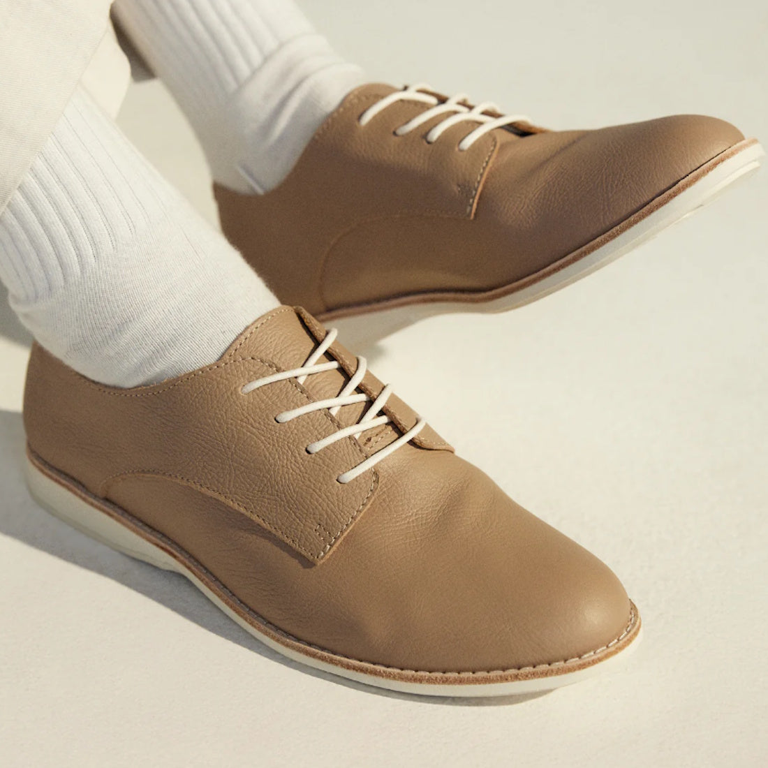 Close-up of a person wearing Rollie Womens Derby Super Soft Clay Leather Shoes with white soles and white socks, standing on a light surface. Only their lower legs and feet are visible., 9781760781552, 9781760781576, 9781760781507, 52452, 52453, 52454
