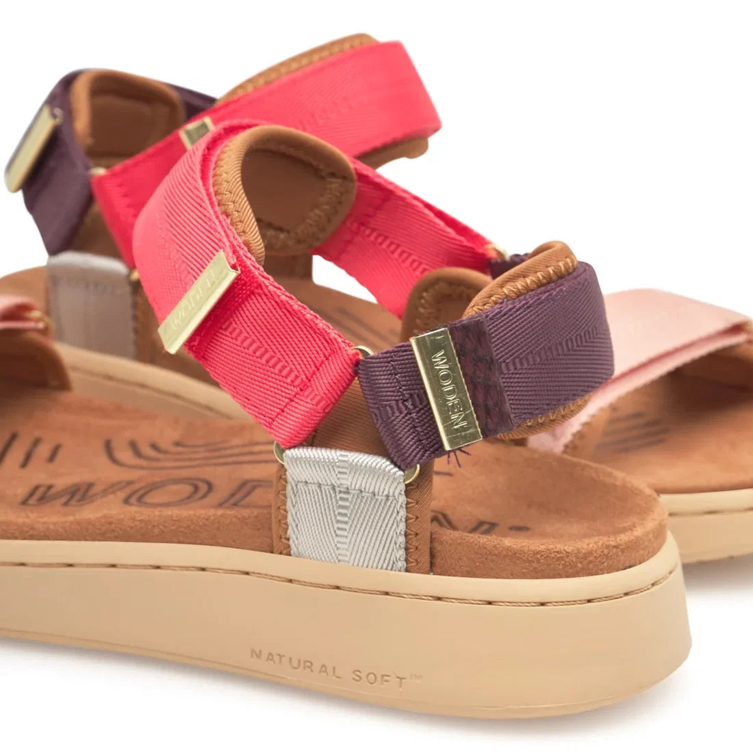 Close-up of the Woden Line Women's 3 Strap Sandal in Flame Multi Red, showcasing two vibrant sandals with adjustable Velcro straps in red, purple, and beige. They feature cushioned tan footbeds and beige rubber soles stamped “NATURAL SOFT”—a comfortable c