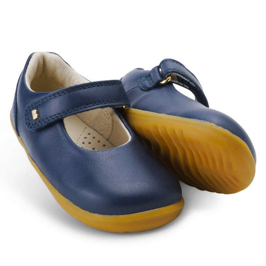 The Bobux Step Up Mary Jane Delight Navy features a leather upper, tan rubber soles, and a hook-and-loop strap, designed for children and shown on a white background.
