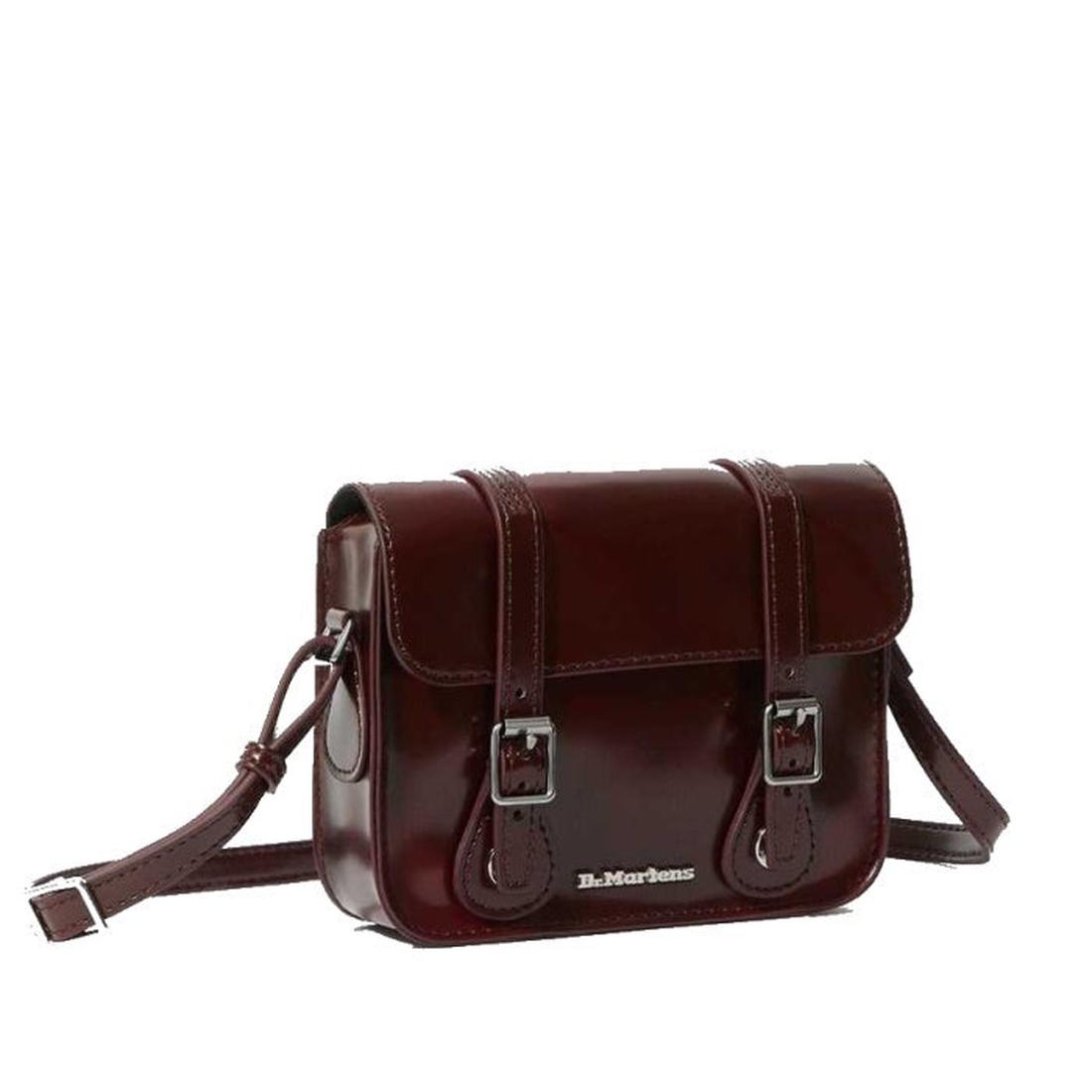 The Dr. Martens 7 Inch Satchel Vegan Cherry Red Oxford Brush is a small, glossy burgundy bag with front buckle straps, an adjustable shoulder strap, and a gold logo—stylish and durable for everyday use.