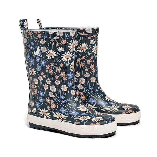 A pair of CryWolf Rain Boots in the Winter Floral Navy design is set against a dark background. These children’s waterproof boots are made from natural rubber and feature a floral pattern with white, blue, and peach flowers. The thick white soles have bla