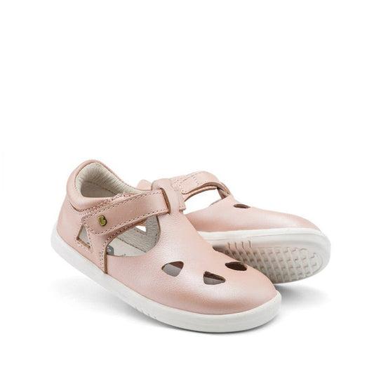 The Bobux IWalk IW Zap II Sandal Pink Shimmer features closed-toe design, cut-out shapes on the toe, a hook-and-loop strap, and white rubber soles. One sandal stands upright, the other is slightly tilted. Perfect for children.
