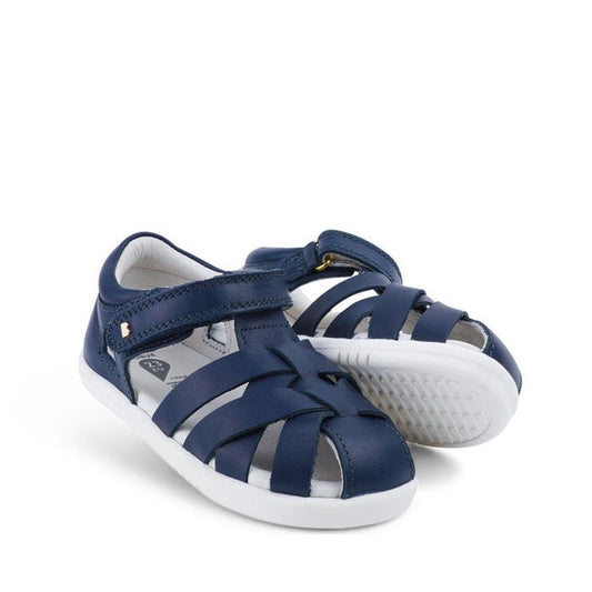 The Bobux Iwalk IW Tropicana II Sandal 638302 Navy is a pair of navy blue toddler sandals with closed toes, white soles, Velcro strap, and Quick Dry Leather, shown against a white background.