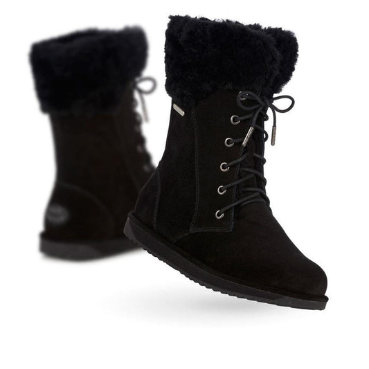 A pair of black Emu Women's Shoreline Sheepskin Waterproof Boots with fur lining, lace-up fronts, and flat soles. One boot stands upright while the other appears slightly blurred in the background.