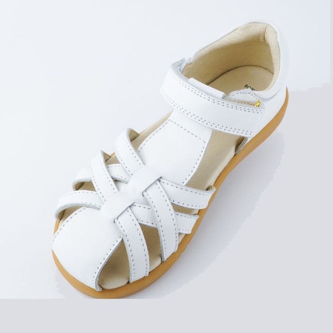 The Bobux Kids + Plus Girls Cross Jump White Leather Sandal 837006 features a closed toe, crisscross straps, hook-and-loop ankle fastener, and light brown rubber sole, shown against a plain light background., 9420068507159, 9420068507166, 9420068507173, 9