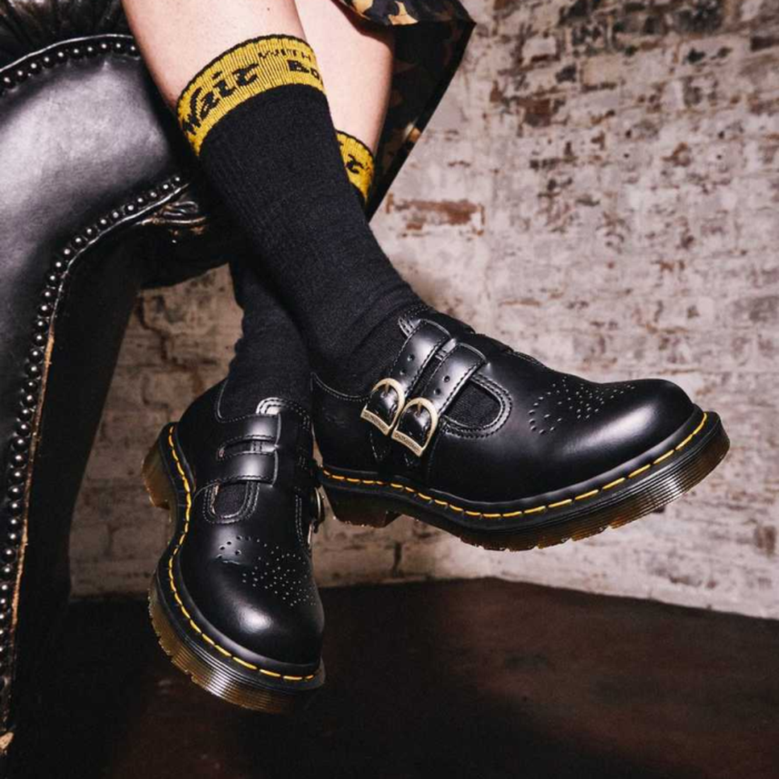 A woman sitting cross legged over the arm of a chaire wearing a pair of dr martens 8065 double strap mary jane shows in black leather. and black crew socks with air wair branding at the top of the sock.,883985051768
883985051775,
883985051782,
88398505179