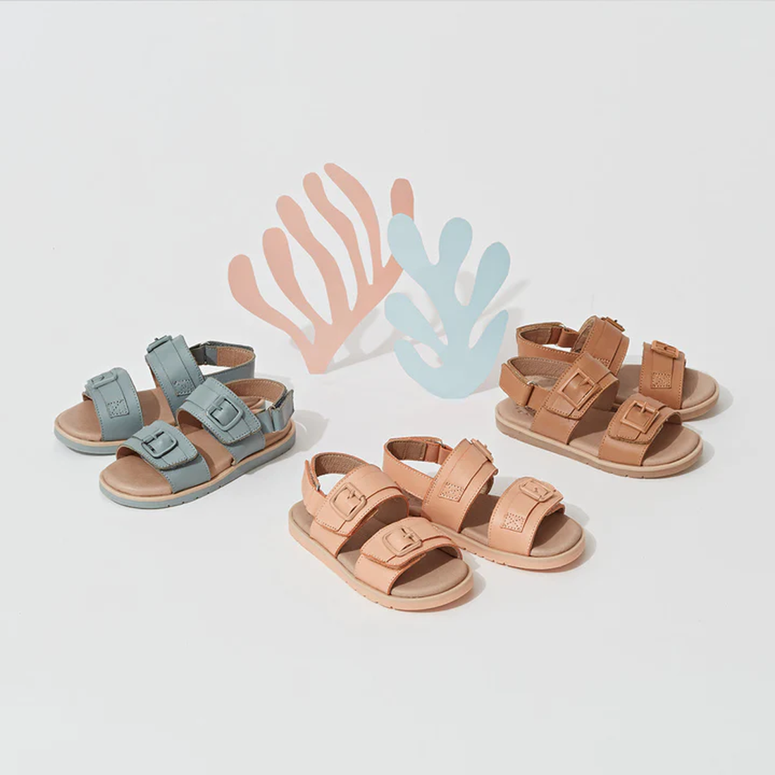 A pair of Pretty Brave Alex Leather Sandal in Coral (sizes 29-33, CLEARANCE NOT RETURNABLE) is displayed on a white surface with abstract coral and plant shapes. The sandal features adjustable velcro straps for a secure fit., 9421036357554, 9421036357561,