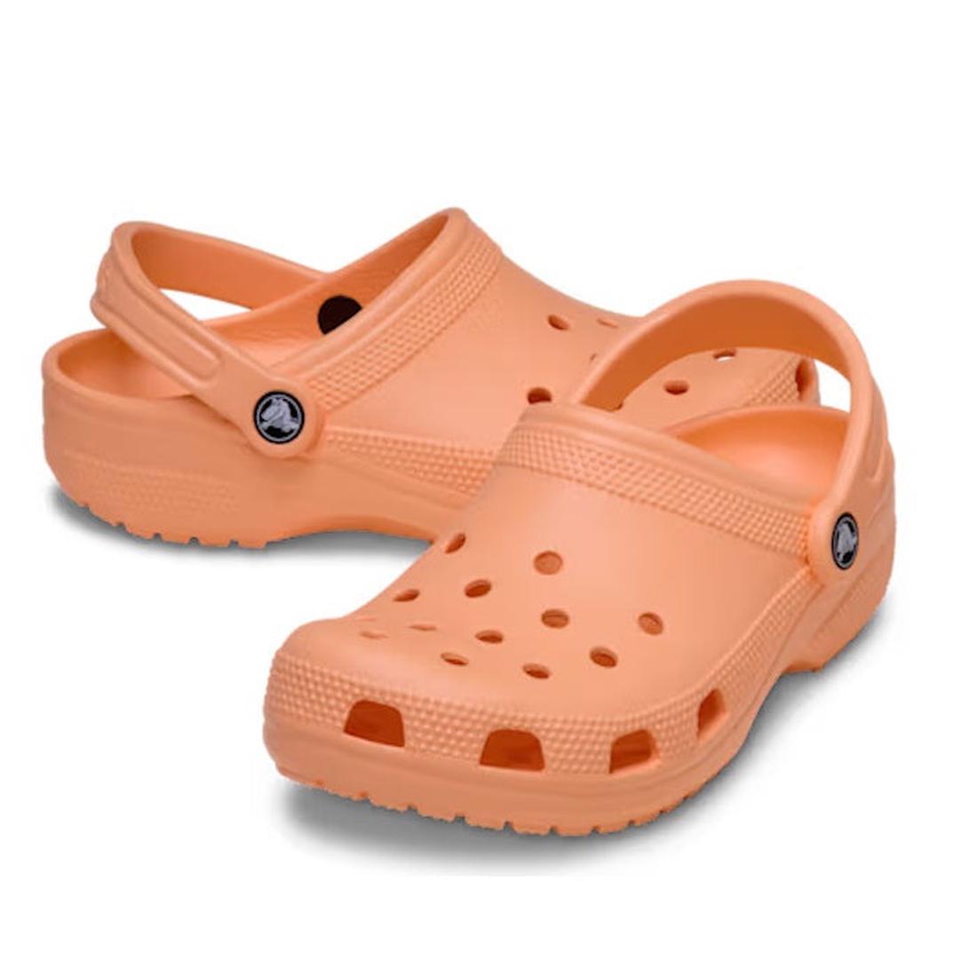 A pair of Crocs - Classic Clog Adults Sunstone Soft Orange with ventilation holes, adjustable heel straps, and textured soles is displayed on a white background.