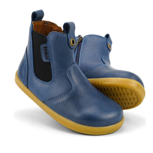 A pair of Bobux Iwalk Jodhpur Ankle Boots Midnight Blue 620849 for toddlers, featuring elastic side panels, brown lining, and light brown rubber soles. One boot stands upright while the other leans to display the sole.