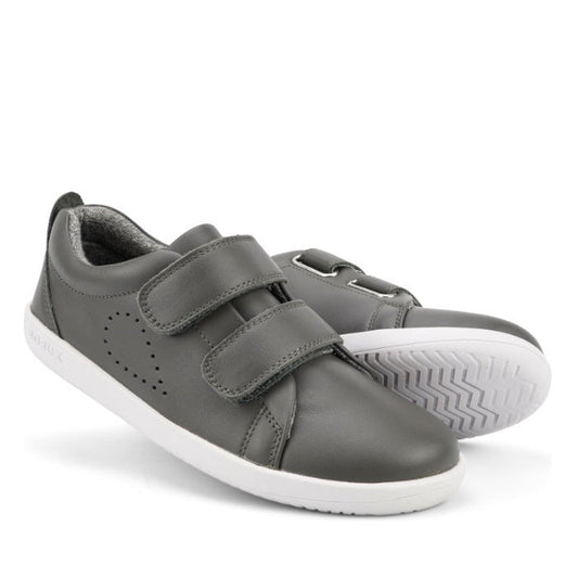 The Bobux Kids + Plus Grass Court Smoke Grey Velcro Trainers 832446 feature two gray velcro straps, white soles, side perforations, and a textured grip—ideal kids’ street shoes for everyday wear.