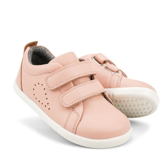 The Bobux Iwalk Grass Court Seashell Pink Leather Trainer features a light pink hue, white soles, perforated side hearts, and double Velcro straps—offering comfort and style for kids’ everyday wear.