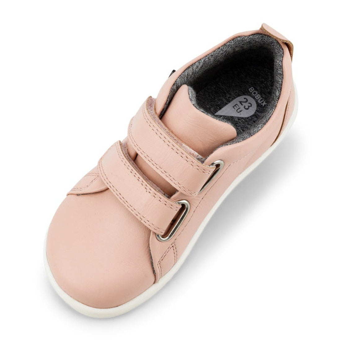 A Bobux Iwalk Grass Court Seashell Pink Leather Trainer (size 23) is shown from above at an angle, featuring a light pink color, two velcro straps, white sole, and dark grey inner lining—perfect sneakers for everyday wear., 9420062078877, 9420075792289, 9