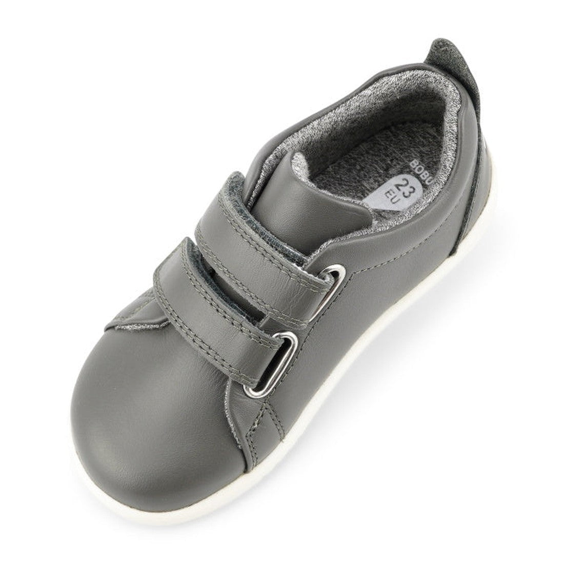 The Bobux Iwalk Grass Court Smoke Grey Leather Trainer 633702 is a kids' sneaker in gray with two Velcro straps, white sole, and soft lining. Shown from an angled top view; inside label shows size 23 EU., 9420068517974, 9420068517981, 9420068517998, 94200