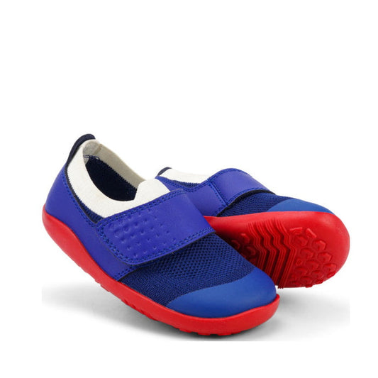 A pair of Bobux Iwalk IW Dimension III Blueberry Red Trainer 638505 kids' slip-on shoes with Velcro straps, blue uppers, red soles, white lining, and textured sole. Lightweight and crafted from twin-face merino knit.