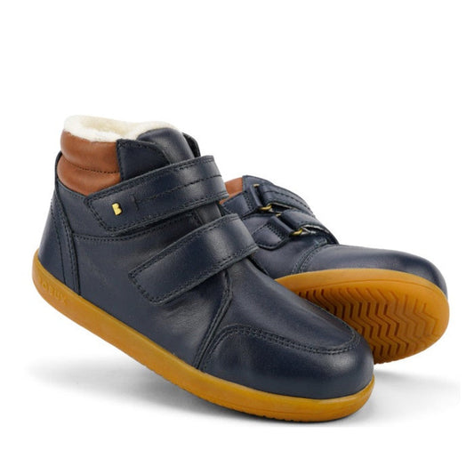 The Bobux Kid+ Timber Arctic WATERPROOF Boot Navy 836003E is a pair of kids' navy leather boots with brown accents, velcro straps, and yellow rubber soles. One boot stands upright; the other is angled to show the tread pattern.