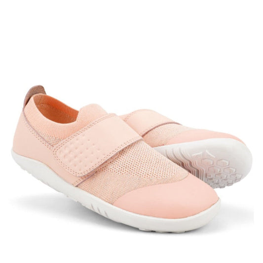 A pair of Bobux Kid+ Lo Dimension III Blossom Pink 838601 slip-on shoes with white soles, textured mesh upper, and a hook-and-loop strap. One kids flexible shoe stands upright; the other is angled to display the sole.