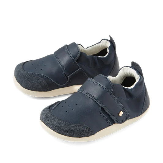 A pair of Bobux XP Explorer Ripple First Walker shoes in navy, featuring beige soles, Velcro straps, and soft suede toe caps. These flexible-soled toddler shoes are perfect for first walkers and are displayed on a white background.