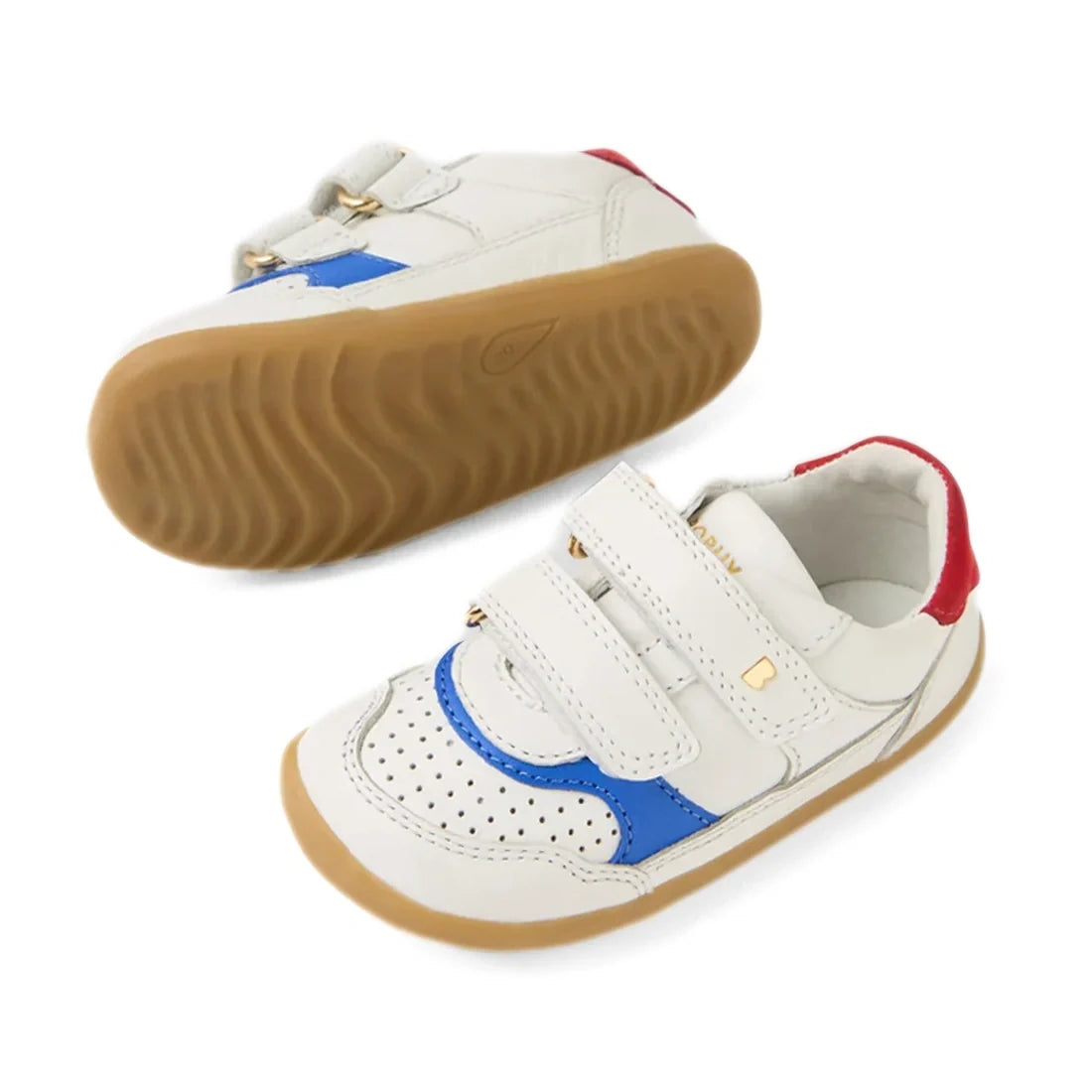 A pair of Bobux SU Step Up Hunter Leather Toddlers Sneakers in White Salsa, featuring white leather uppers, tan rubber soles, blue and red accents, and two velcro straps on each shoe. One shoe is upright while the other displays the sole—perfect first wal