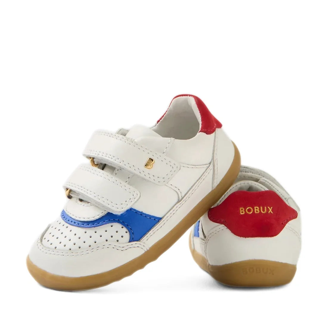 A pair of Bobux SU Step Up Hunter Leather Toddlers Sneaker in White Salsa, featuring white leather with blue and red accents, brown soles, and two velcro straps. Gold “BOBUX” branding appears on the heel and side, making these stylish first walker shoes i