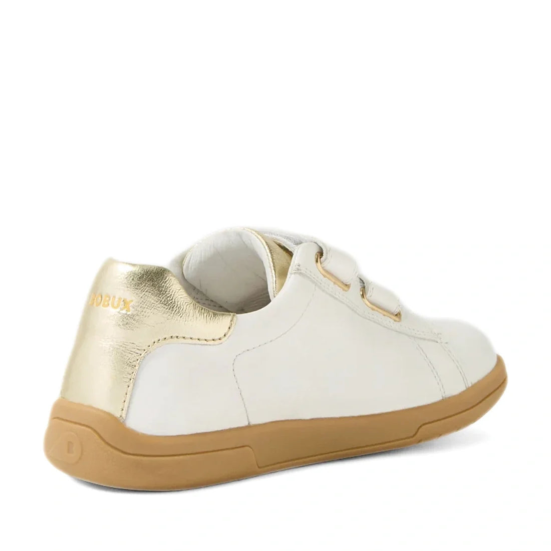 The Bobux Kid+ Plus KP Maverick Leather Sneaker in White Gold features a white upper, light brown sole, gold heel accent, and two velcro straps, shown from the back left—ideal for those looking for comfortable kids’ sneakers with an adjustable strap desig