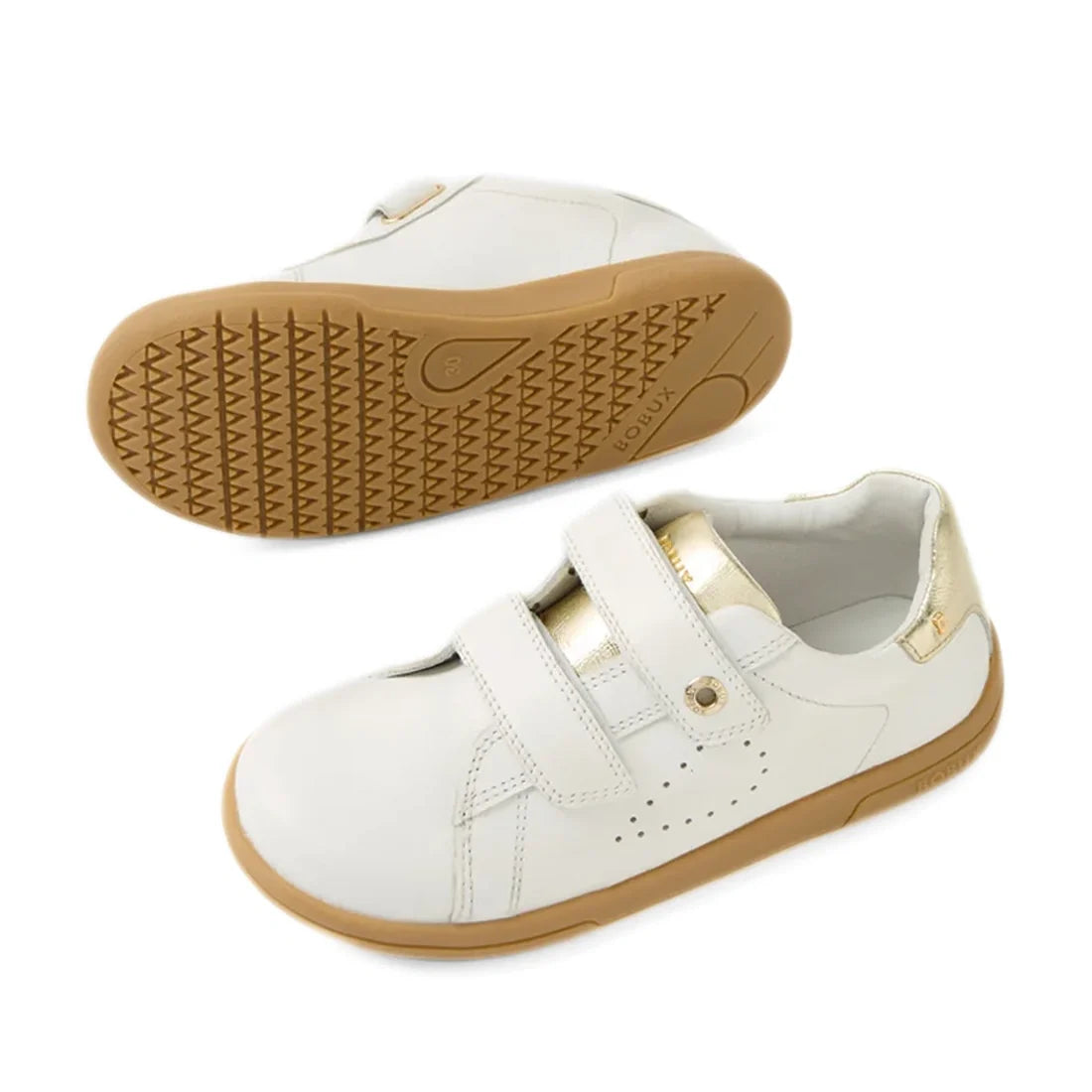 The Bobux Kid+ Plus KP Maverick Leather Sneaker in White Gold features two adjustable velcro straps, stylish gold heel accents, and tan rubber soles. These comfortable leather children’s sneakers are designed for everyday adventures. One shoe is displayed