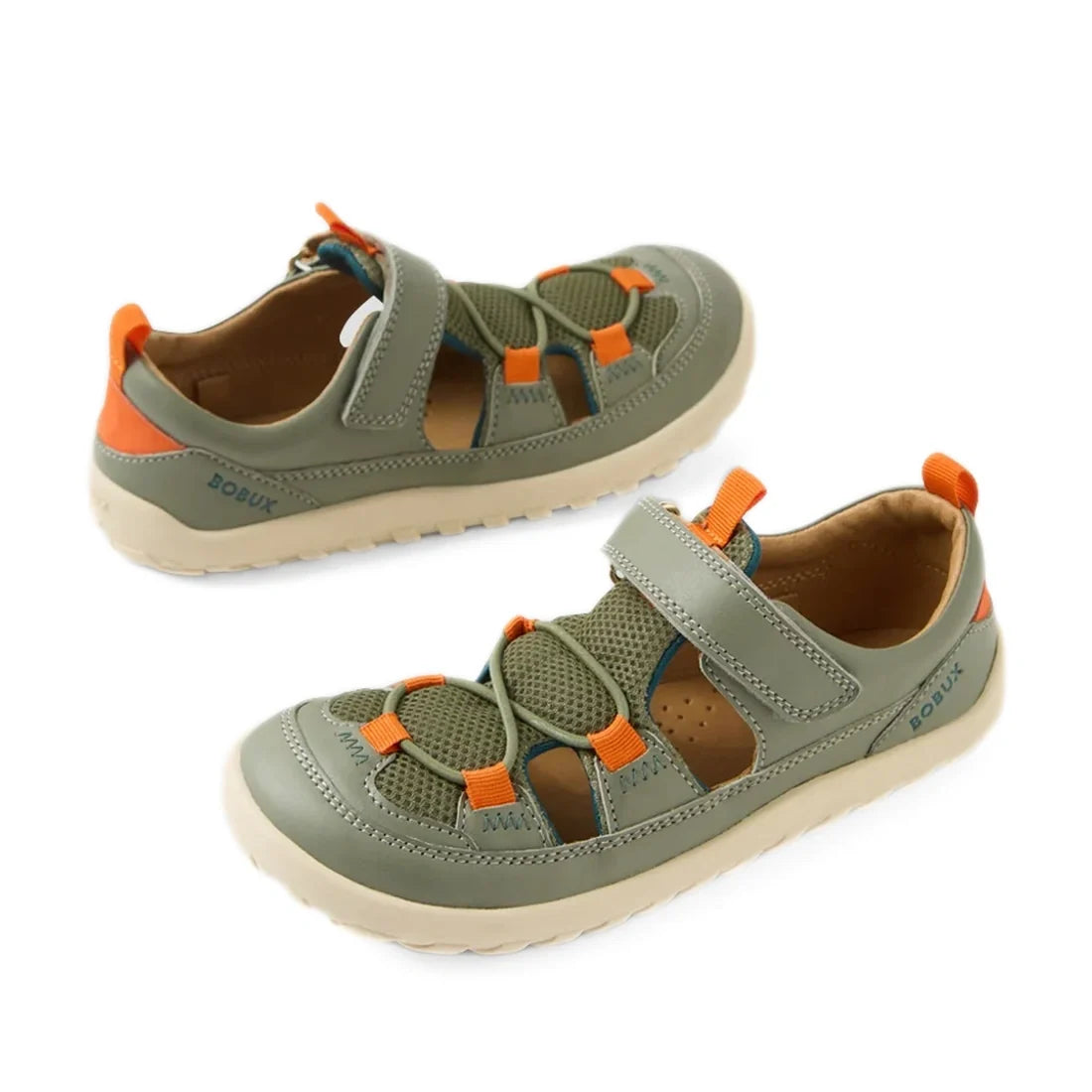 Two Vetiver Green Bobux Kid+ KP Rocky closed-toe leather barefoot sandals for kids, featuring beige soles, orange and olive mesh and leather details, adjustable straps, and orange pull tabs at the back. Designed to support natural foot movement, both sand