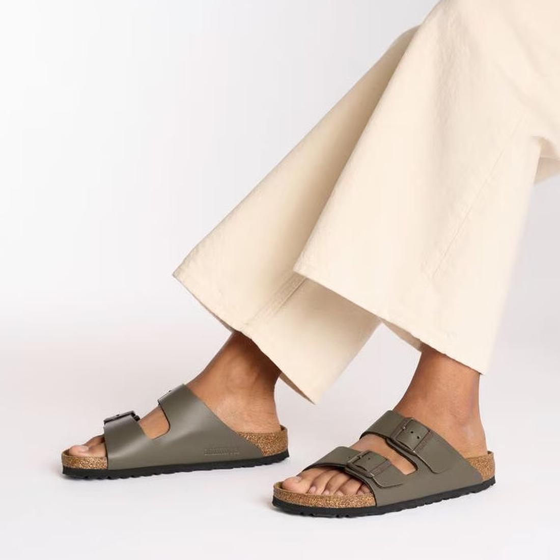 A person in wide-legged cream pants and Birkenstock Arizona Smooth Natural Leather sandals in Concrete Grey (Regular Width) stands against a plain white background., 47484, 4066648922902, 4066648922940, 4066648922988, 4066648923022, 4066648923060, 4066648