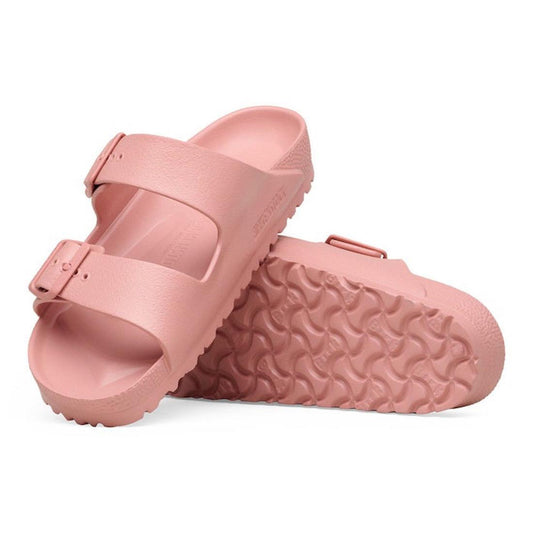 The BIRKENSTOCK Arizona EVA Pink Clay Narrow Width sandals feature two adjustable straps and textured soles. One sandal stands upright, while the other is on its side to display the anatomically shaped footbed and tread pattern.