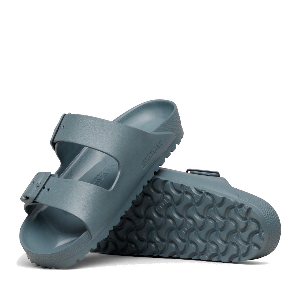 A pair of BIRKENSTOCK Arizona EVA Basalt Grey sandals, REGULAR width, featuring two adjustable straps and buckles; one sandal stands upright showing the textured sole, while the other lies flat displaying its top side.