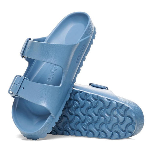 A pair of Birkenstock Arizona EVA Elemental Blue Narrow Width sandals with two adjustable straps—one shown upright, the other on its side to reveal the waterproof, textured sole featuring a wave-like pattern.
