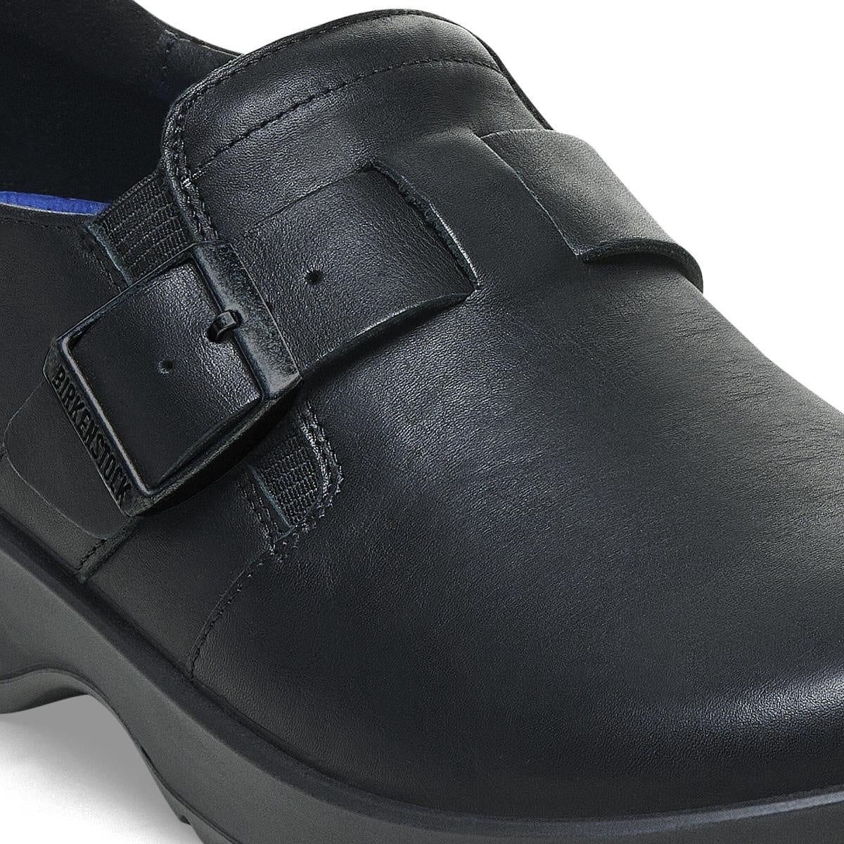 A close-up of the BIRKENSTOCK Caris Pro Slip Resistant Black Leather Shoe showcases its ergonomic design, low heel, strap and buckle detail, visible stitching, and textured slip-resistant sole—ideal for occupational wear.