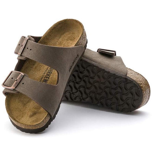 A pair of Birkenstock Kids Arizona Mocca Birkibuc Narrow Slides, featuring two buckled straps, contoured cork footbeds, and black textured soles. One slide is upright; the other is propped up to display the sole.