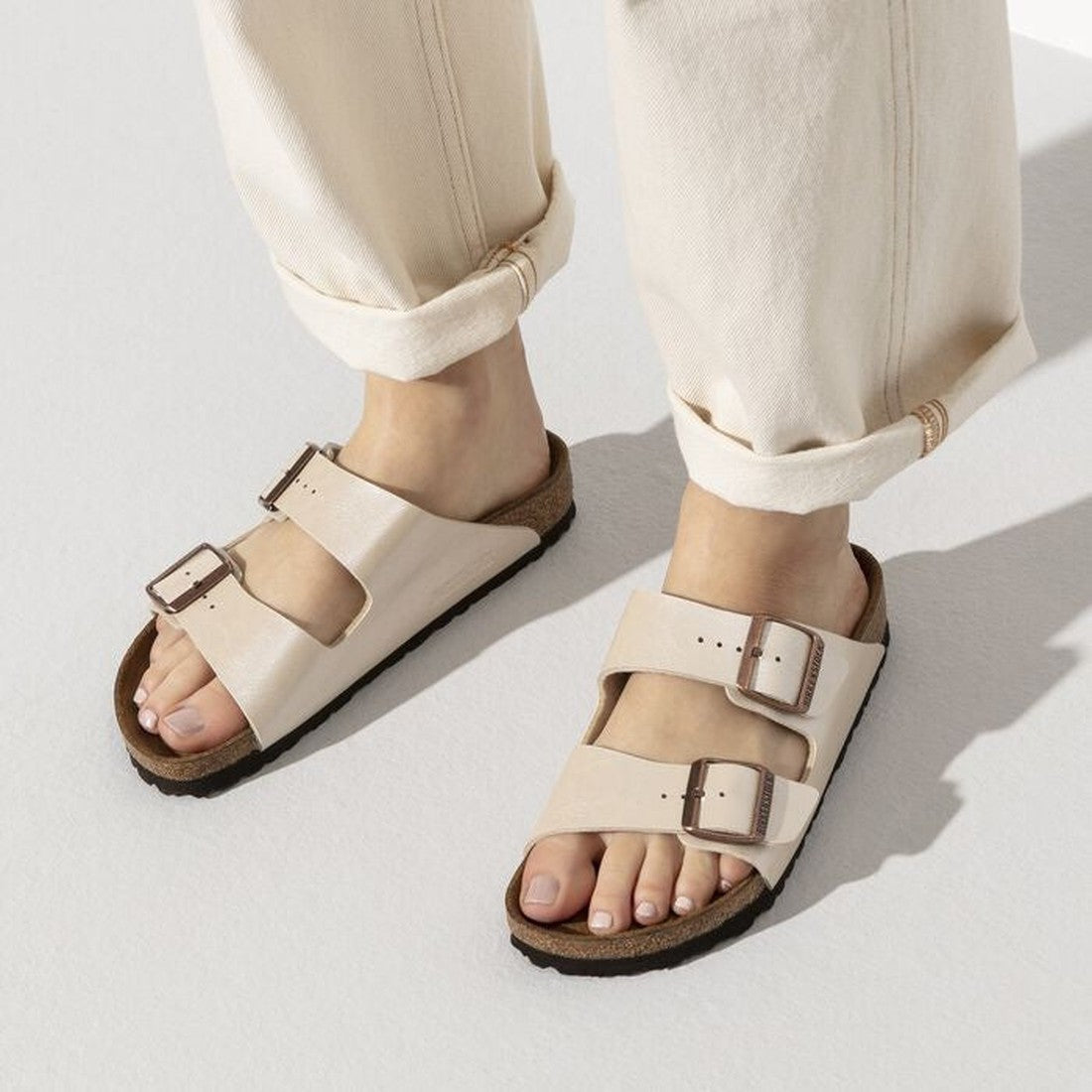 Arizona 2 strap sandals in a warm pearlised white with gold buckles on a woman wearing rolled up cream coloured pants with a top down view of both feet.,4044477107172,4044477107196,4044477107219,4044477107233,4044477107257,4044477107271,,,,,,,
, 41345, 41