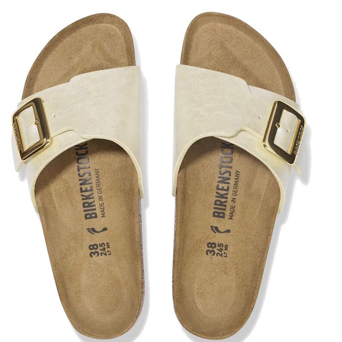 A pair of Birkenstock Womens Catalina Cushion Buckle Birko Flor sandals in pearl white with large gold buckles, supportive cork-latex footbeds, brown soles, sizing details, and "Made in Germany" labels is viewed from above., 4066648995265, 4066648995302, 