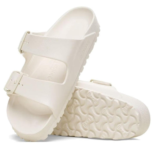 The Birkenstock Arizona EVA in Eggshell Off White (Narrow Width) features two adjustable buckle straps, a textured sole, and a contoured EVA footbed, with one sandal upright and the other showing its sole.