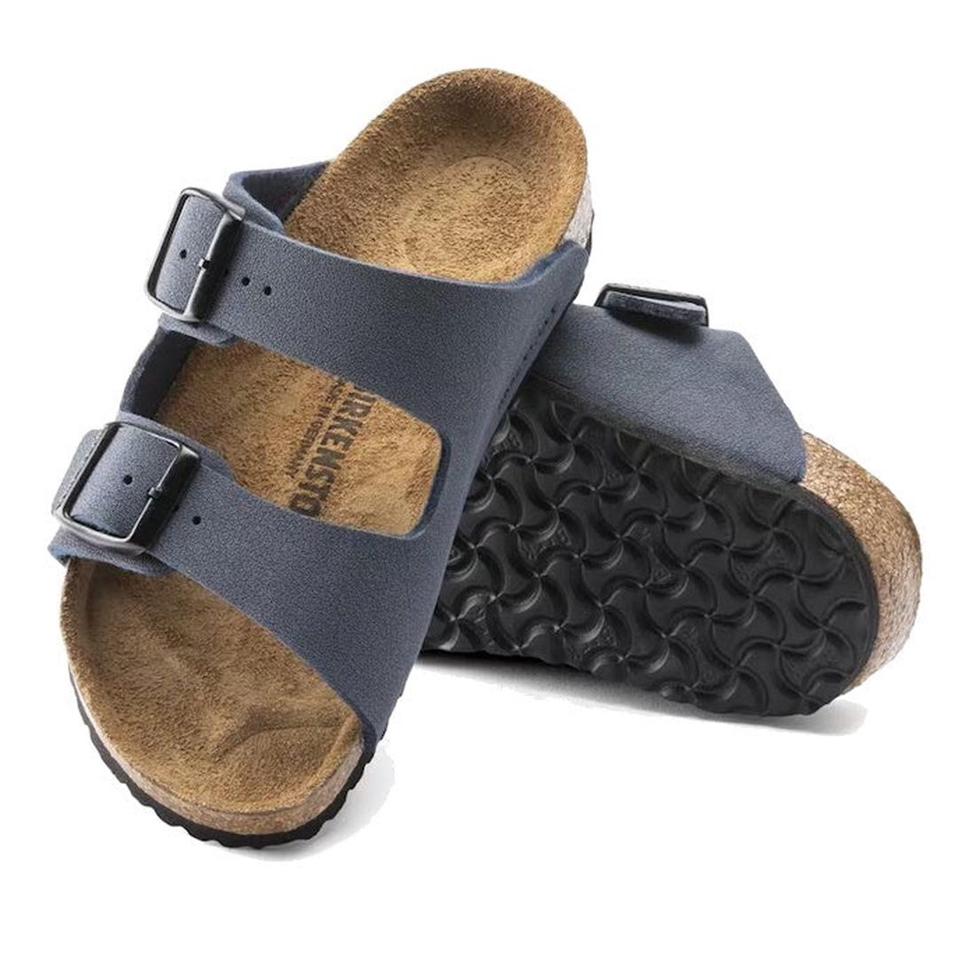 A pair of Birkenstock Kids Arizona Navy Birkibuc Narrow Slides featuring two adjustable buckles and a comfy cork-latex footbed. One sandal lays flat, the other is propped to display the textured black sole.