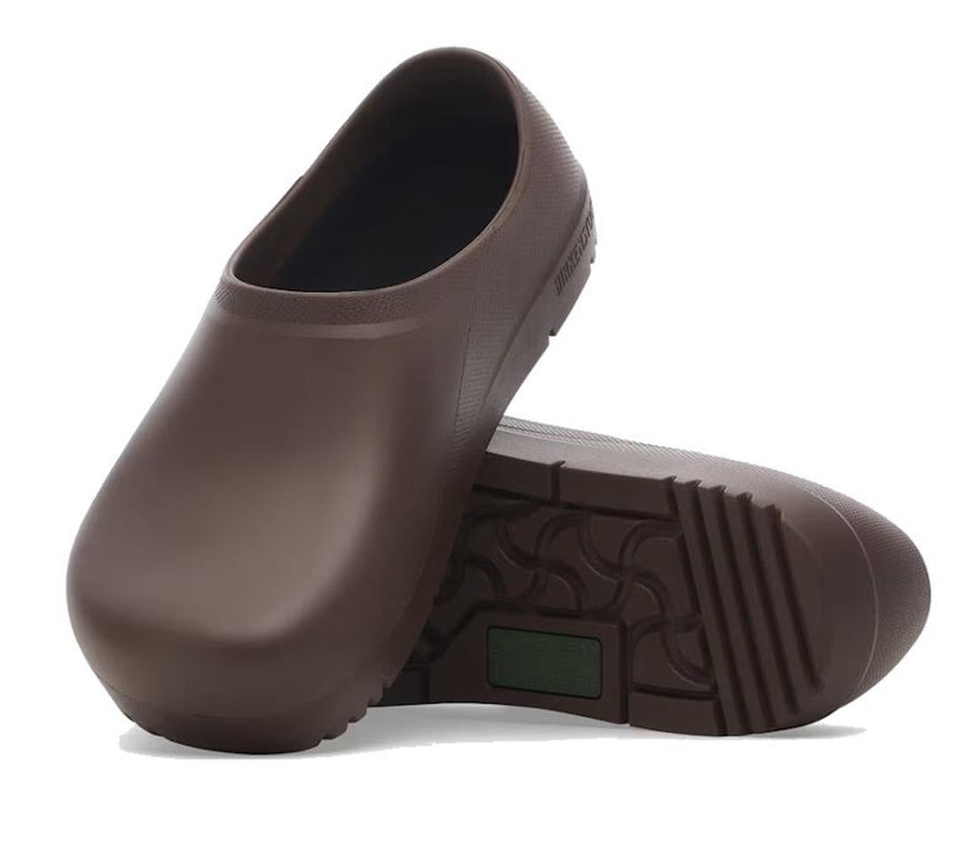 A pair of Birkenstock Profi Birki 2.0 Polyurethane Mocca Brown Regular Width clogs, one upright and one on its side to show the textured tread and smooth design, ideal for kitchen use.