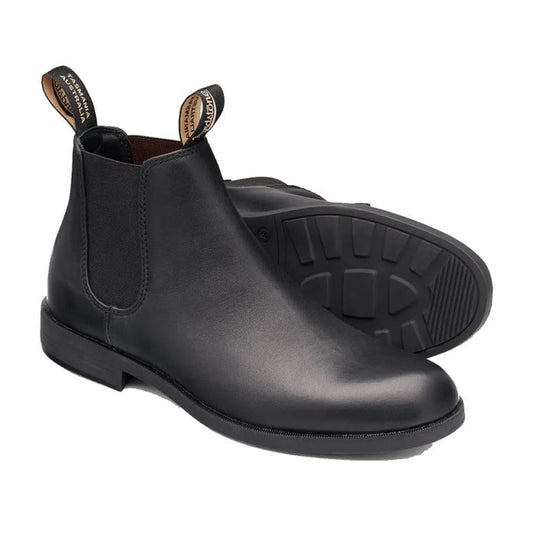 A pair of Blundstone 1901 Mens Dress Black Boots, tapered fit with pull tabs and elastic side panels, is shown on a white background. One boot stands upright; the other reveals its treaded sole. Versatile ankle boots for any occasion.