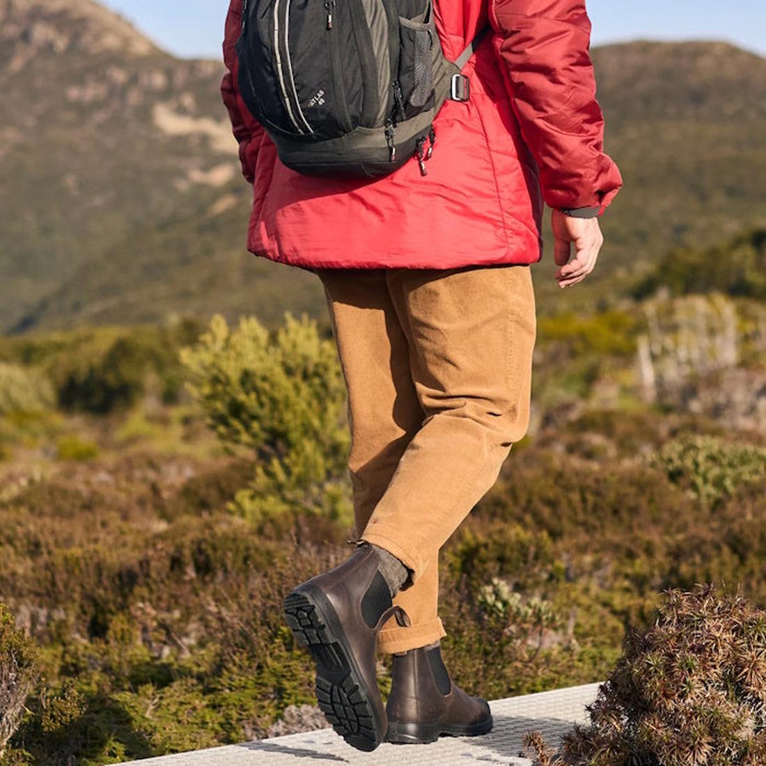 A parent strolls on a green hill trail wearing Blundstone 2340 rich brown Chelsea boots with sturdy sole and easy pull-on sides.  ksnz, 9315891562553, 9315891562577, 9315891562591, 9315891562614, 9315891562638, 9315891555692, 9315891562669, 9315891562683, 9315891562690