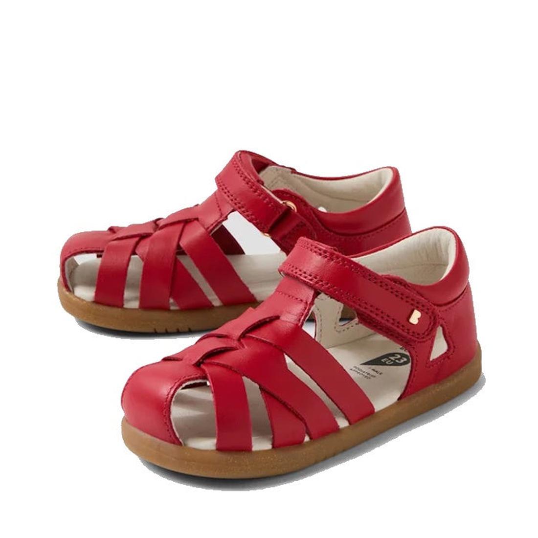 The Bobux Iwalk IW Tropicana II Salsa Red Leather Sandal features enclosed toes, open sides, crisscross straps, tan rubber soles, and adjustable hook-and-loop ankle closures for a secure fit for toddlers.