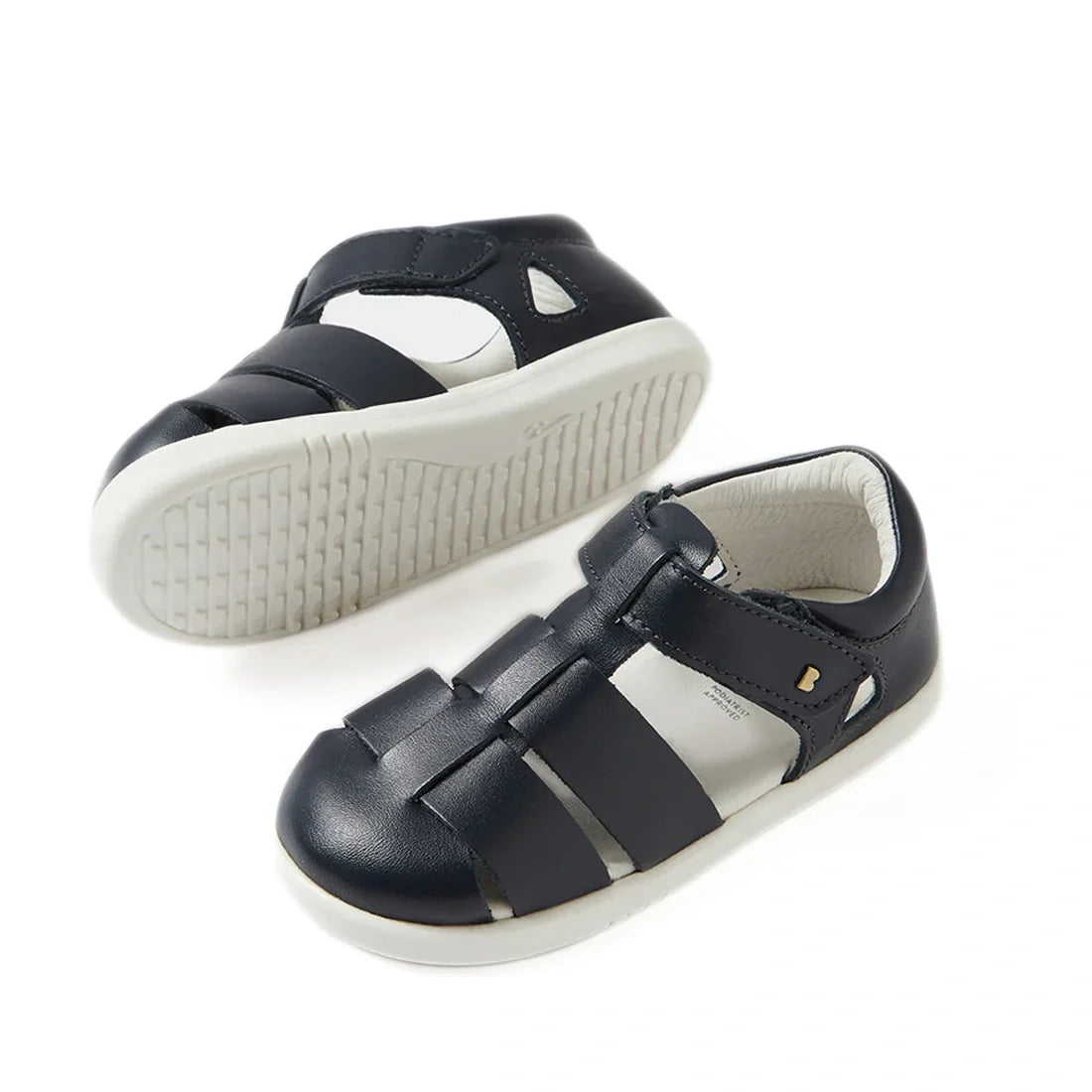 A pair of Bobux IWalk Tidal Closed Toe Quick Dry Sandals in navy (model 634404A) for kids, featuring a unisex design with white soles, crafted from quick-dry leather and equipped with adjustable Velcro straps, displayed on a white background.