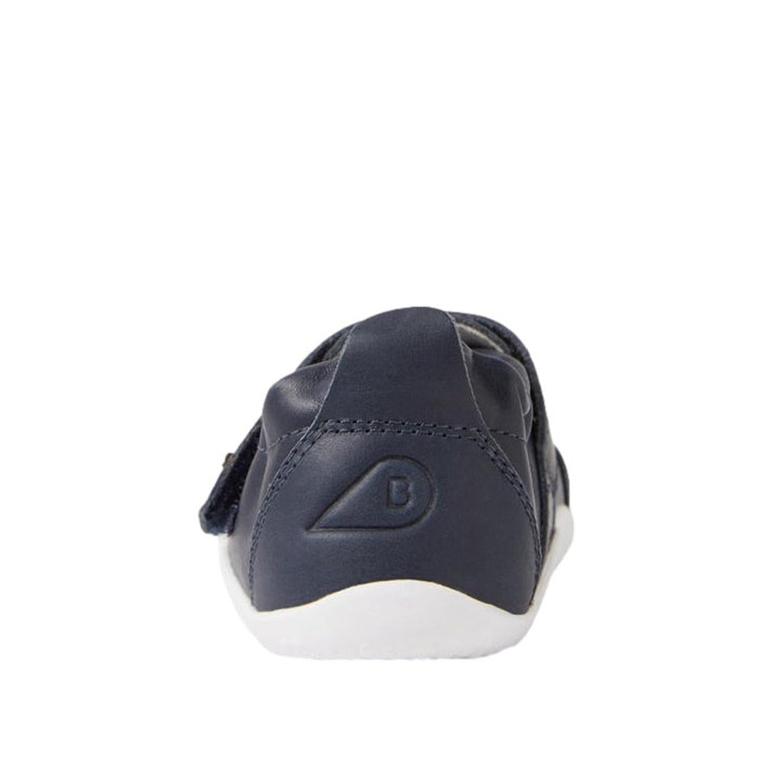 The Bobux XP Explorer Beau First Walker Sandal in navy is a toddler leather shoe with a flexible white sole, shown from the back and featuring a stitched B logo on the heel., 9420068568808, 9420068568815, 9420068568822, 9420068568839